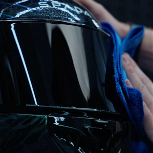 someone cleaning the visor of a spada motorbike helmet with a microfibre cloth